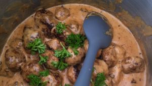 Brun sås En blå slev i en bytta med köttbullar och brun sås.