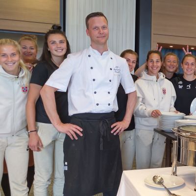 Anders Svahnström iklädd kockdräkt står tillsammans med en del av det norska damlandslaget i fotboll.