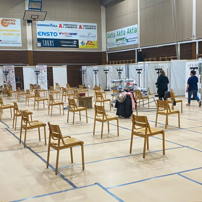 En stor idrottssal omgjord till vaccineringsställe. Längs två väggar finns vaccineringsbås. På golvet står stolar i rader.
