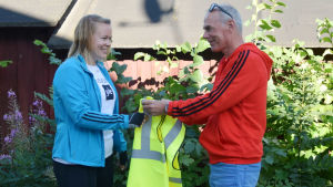 Vilken överraskning! Motionsföreningen Topptrim, representerad av Ulf Heimberg, donerar en reflexväst till mig. Malin Valtonen tar emot en gul reflexväst av Ulf Heimberg från motionsföreningen Topptrim.