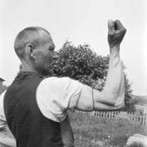 "Bryta märling", Strömfors, Kungsböle 1929. En man försöker bryta en märling med sin armmuskel. Fotot är taget 1929 i Strömfors, Kungsböle.