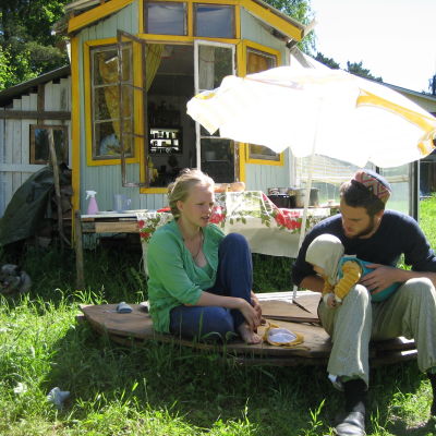 Vilma och Per-Viktor utanför sitt mobila hus, ett blått trähus med hjul under. På bilden finns också familjens förstfödda baby.