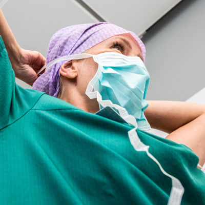 Sjukskötare knyter fast ett ansiktsskydd i sjukhusmiljö.