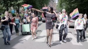 Dokumenttiprojekti: Kelet. Kelet går mitt i ett Pridetåg i Helsingfors och håller i prideflaggan.