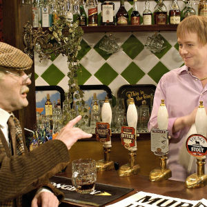 Norman (Frank Boyle) ja pubin isäntä Jules (Eamonn Riley) jutustelevat tiskin ääressä.