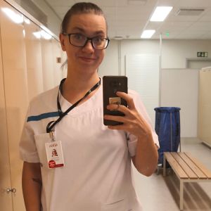 En kvinna i sköterskeuniform tar en selfie i ett omklädningsrum.