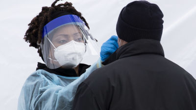 En sjukskötare i skyddsutrustning gör en coronatest på en patient.