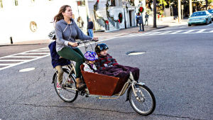 Sandra vill gärna se fler lastcyklar i stadsbilden. En kvinna cyklar men två barn sittandes fram i en korg och ett barn på pakethållaren.