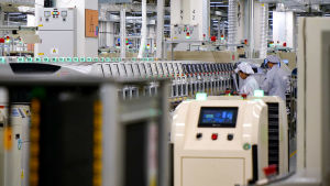 I Huaweis södra fabrik i Shenzhen tillverkas P30-smarttelefoner. År 2013 jobbade 83 personer vid en sån här enhet, i dag är de 17 till antalet. En rad med maskiner i en fabrik. Borta till höger står två anställda.