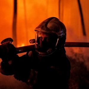 Brandman sprutar vatten mot en skogsbrand i Gironde i Frankrike medan elden härjar skogen i bakgrunden.