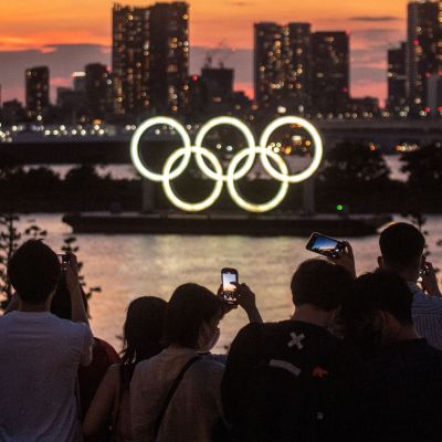 Ihmiset kuvaavat valaistuja olympiarenkaita auringon laskiessa Tokiossa 22. heinäkuuta.
