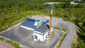 Värmeverket i Bäljars kan i framtiden ersätta pannorna i Tallmo. Två stora vita hallaktiga byggnader och en hög skorsten. Fotat uppifrån. Byggnaderna står på en asfalterad plan och omges av vägar och avverkad skog.