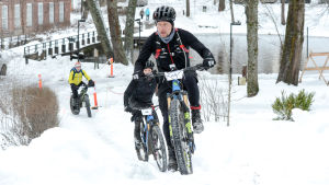 Tomi Paavola tar sig uppåt. Tomi Paavola cyklar i vinterräng upp för en backe.