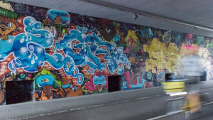 Längs med cykelvägen Banan i Helsingfors finns det flera muraler. Den här som finns under en bro är gjord av gatu- och graffitikonstnärerna som går under artistnamnen Os Gemeos och EGS. En väggmålning under en bro längs en cykelväg.
