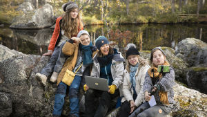 Fotarit. Ryhmä nuoria istuu kalliolla ja ottaa yhteistä selfietä.