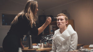Charlotta Barman fixar sminket på Emil Strandell före en filmtagning. En kvinna sminkar en man inför en filminspelning.
