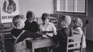 Historia: Sodan lapset. Mustavalkea kuva, jossa lapset kokoontuneet luokkahuoneessa pöydän äärelle
