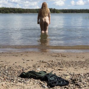 Roosa Vastamäki on kahlannut melkein polvien syvyyteen merelle. Rantahiekalla on hänen musta-vihreät rintaliivinsä.