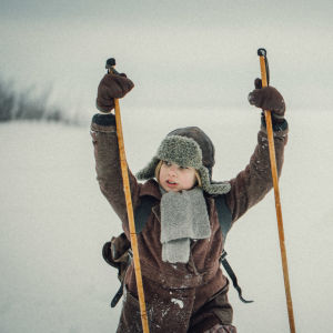 Pieni tyttö 1930-luvun vaatteissa nojaa suksisauvoihinsa ja katsoo jonnekin. Kuva elokuvasta Lakana.