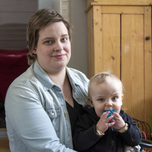En kvinna som sitter på golvet i sitt vardagsrum, med ett litet barn i famnen.