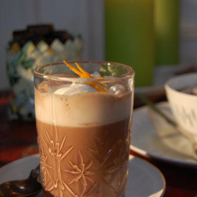 Ett glas med varm choklad toppat med vispgrädde och rivet apelsinskal.