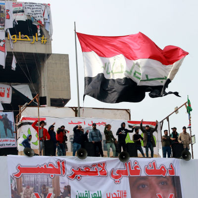 Irakiska demonstranter håller irakiska flaggan uppe på taket på en byggnad nära Tahrir-torget i centrala Bagdad.