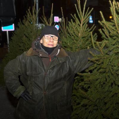 Joulukuusikauppias Nea Sipola esittelee perinteistä joulukuusipuuta keskellä Tammelan torilla aamuhämärissä. 