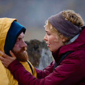 Ingrid ställs mellan två dåliga alternativ. Erik i gul regnrock utmatad och frusen med Ingrid som håller om hans kinder ute på stranden.