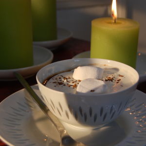 En kopp med varm choklad toppad med marshmallows, vispgrädde och lite kaffepulver.