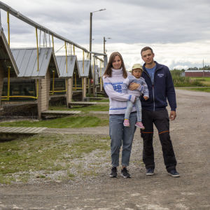 En man och en kvinna som håller ett barn i famnen står framför en rad av hus där rävar förvaras.