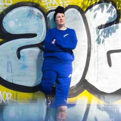 Rika Jylhä nojaa graffitiseinää vasten.