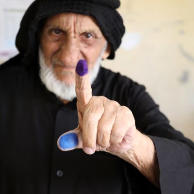 En äldre irakisk man visar upp ett färgat pekfinger och en tumme som bevis på att han har röstat.