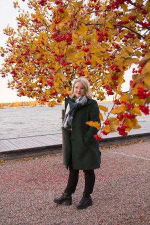 Från och med november börjar Linda aktivt lyssna på julmusik. En blond kvinna med glasögon. Står framför en rönn med röda bär. I bakgrunden syns havet.