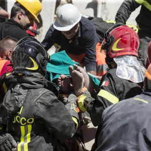 Flera räddningsarbetare hjälps åt att få en räddad man bortförd på bår i Fonte del Campo nära Accumoli