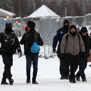 Kaksi poliisia saattaa neljää turvapaikanhakijoita lumista maisemaa vasten Vartiuksen rajanylityspaikalla.