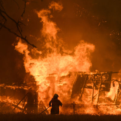 En brandman står i förgrunden, i bakgrunden brinner ett hus.