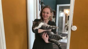 Stella Törnroth är glad över att ha mer tid för olika hobbyer efter flytten. Stella Törnroth står i en dörröppning med en katt i famnen
