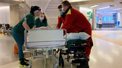 Sjukvårdspersonal transporterar en patient i sin säng i en korridor.