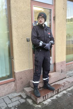 Vid kontoret i Lojo har väktaren tidvis fått stå utanför och begränsa antalet kunder som släpps in. En väktare i svarta kläder står utanför en dörr framför ett gult rappat hus.