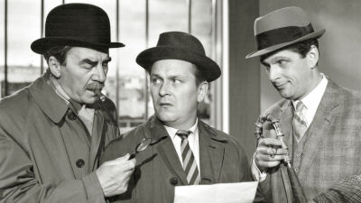 Svartvit bild från filmen Komisario Palmu. Tre män samtalar kring ett vitt papper. 
