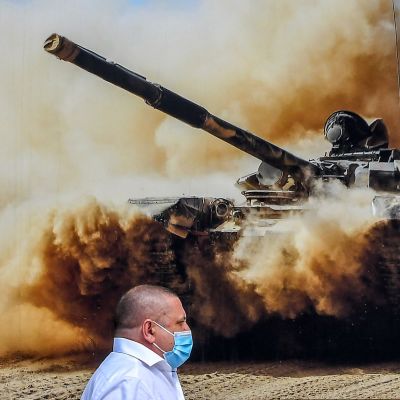 En man med ansiktsskydd framför en storbild på en rysk pansarvagn.