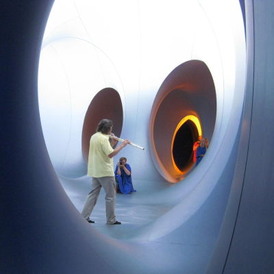 En man i gul skjorta spelar flöjt i Colourscape, ett konstverk man kan gå in i och genom runda gångar.