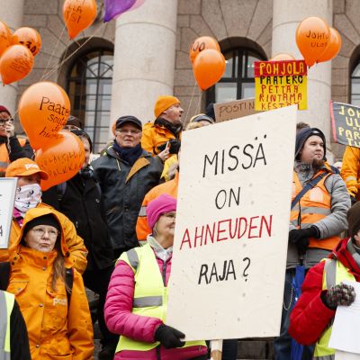 Postanställda i orange jackor och neongul västar står på riksdagshusets trappor med skyltar och ballonger och demonstrerar.