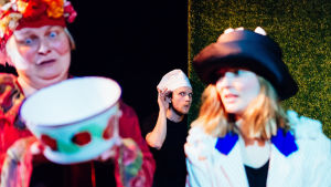 Två mödrar gör upp om barnens framtid. På bilden Niina Hosiasluoma och Janna Räsänen med Juho Keränen smyglyssnande i bakgrunden. Foto från Miten kävi ja terveisiä på Teater Takomo.