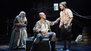 En hotfull gäst. Bill Bones (Niklas Häggblom) lägger ut texten för Farmor Hawkins (Sue Lemström) och Jim (Misa Lommi). Foto från Skattkammarön på Svenska Teatern.