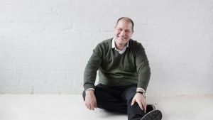 Stuba Nikula, chef för Helsingfors evenemangsstiftelse är kritisk till exitplanen. Stuba Nikulan muotokuva, jossa tämä istuu lattialla nojaten valkoiseen tiiliseinään.