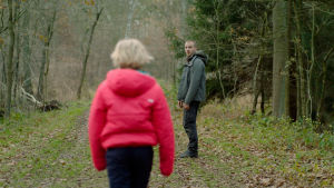 Benni ja Micha metsässä. Benni (Helena Zengel) on selin kameraan kävelemässä metsätietä. Micha (Albrecht Schuch) odottaa häntä vähän edempänä ja katsoo kameraan päin. Kuva elokuvasta Systeeminmurskaaja (Systemsprenger)