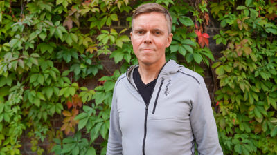 Roy Nielsen står framför växter på en vägg och tittar in i kameran.