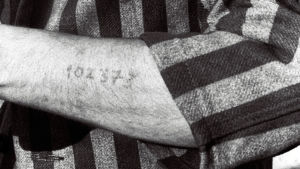 Tunnusnumero tatuoituna keskitysleirivangin käteen. Kuva elokuvasta Yö ja usva