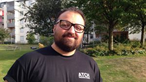 Fältarbetaren Ata Hosseini säger att det finns ett misstroende mot myndigheter, som kan vara en av orsakerna till exempelvis stenkastning mot polis. Porträttbild på fältarbetare i Stockholm, Ata Hosseini. I bakgrunden en grönskande innergård och höghus.